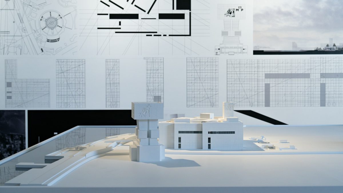 Maquette architecturale posée devant des plans de construction affichés au mur