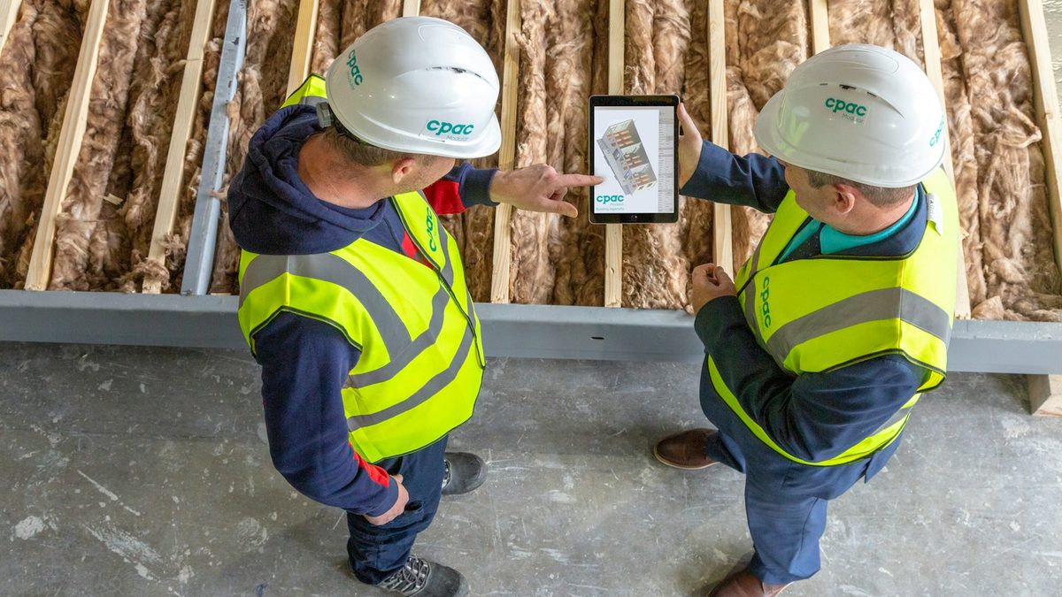 Deux compagnons en casque et gilet consultent des plans sur une tablette, sur un chantier en cours.