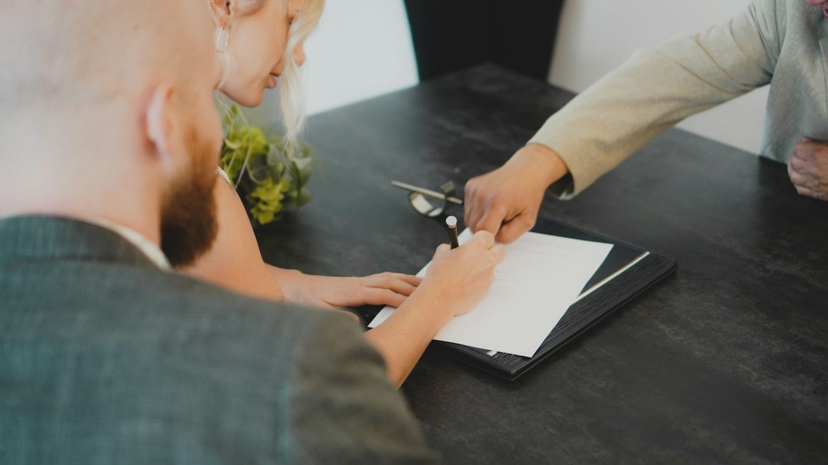 Un couple signe un document à un bureau, face à un professionnel qui lui présente l'acte.